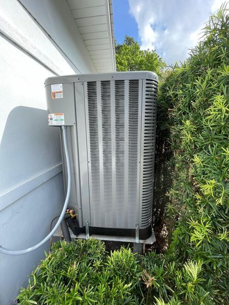 An outdoor air conditioning unit next to a building and bushes.