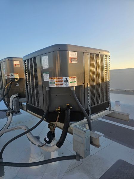 Two gray rooftop air conditioning units against a blue sky, pipes visible, on a white surface.