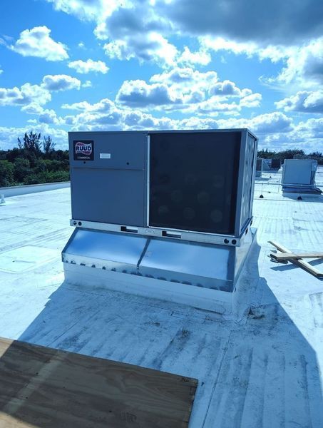 Rooftop HVAC unit on a white flat roof under a blue sky with scattered clouds.