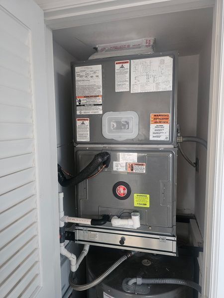 HVAC unit in a closet. Gray metal components, pipes, and warning labels are visible.