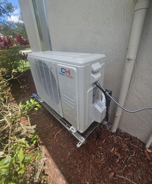 White CH air conditioning unit on a metal stand next to a wall with beige mulch.