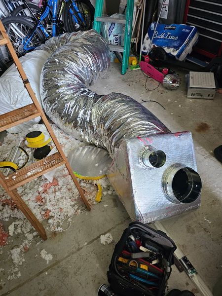 Ductwork and a toolbox in a garage. A flexible vent hose is connected to a rectangular metal box.