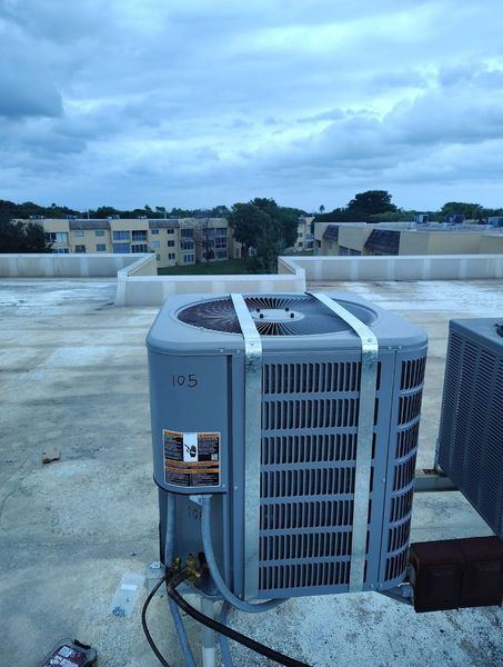 AC unit on a rooftop, with a cloudy sky and apartment buildings in the background.