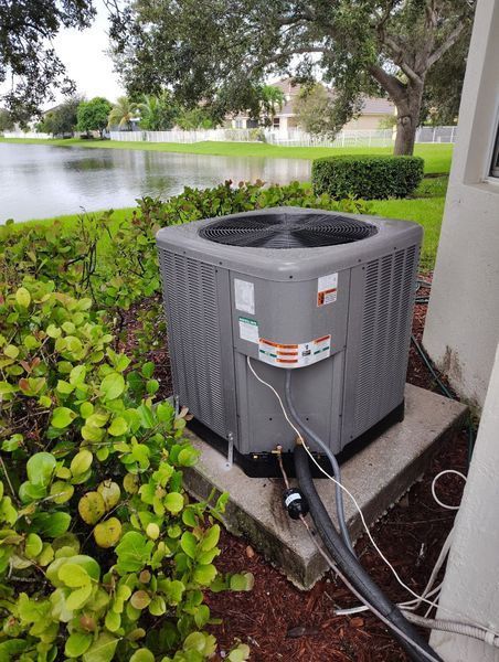 Air conditioning unit outside a house near a lake, surrounded by greenery.