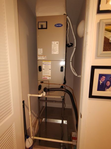 HVAC unit in a closet. Beige rectangular unit with pipes and a condensate drain. Closet has white walls and door.