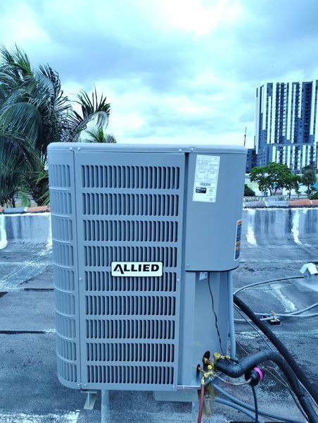 Allied air conditioning unit on a rooftop with a cloudy sky and cityscape in the background.