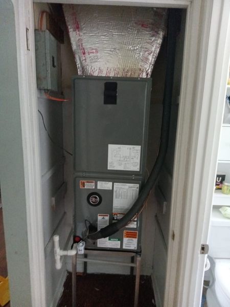 Furnace unit inside a closet, silver ductwork, with electrical box on wall.