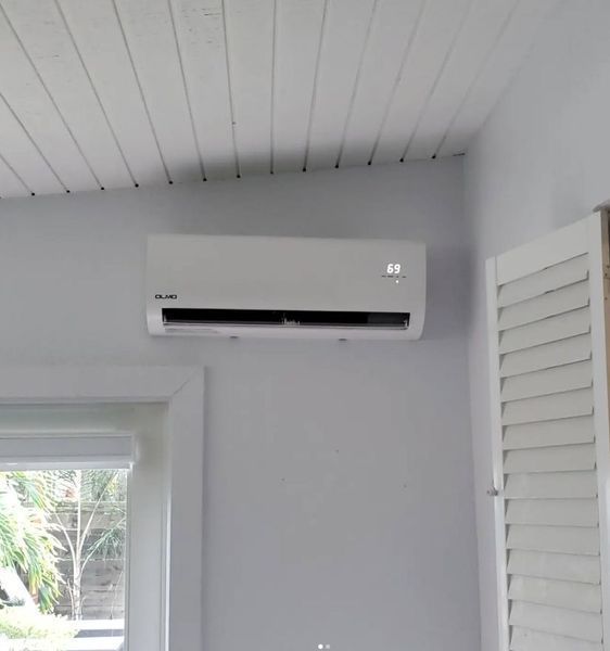 White wall-mounted air conditioning unit in a room with a window and shutter.