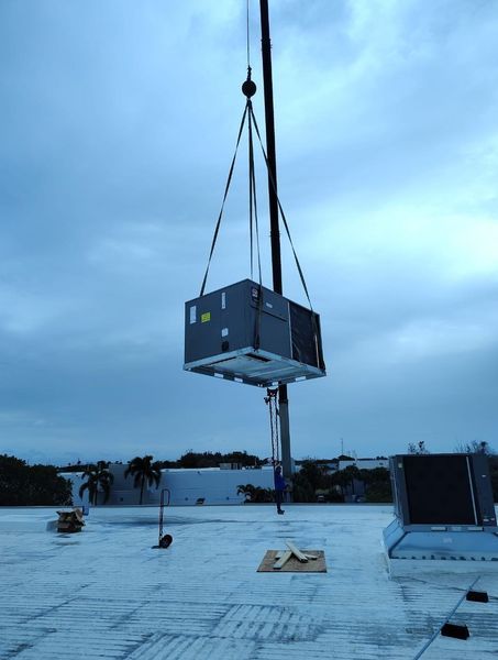 Crane lifting a large HVAC unit onto a rooftop on a cloudy day.
