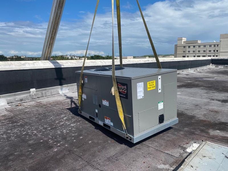 HVAC unit being lifted by crane onto a rooftop under a blue sky.
