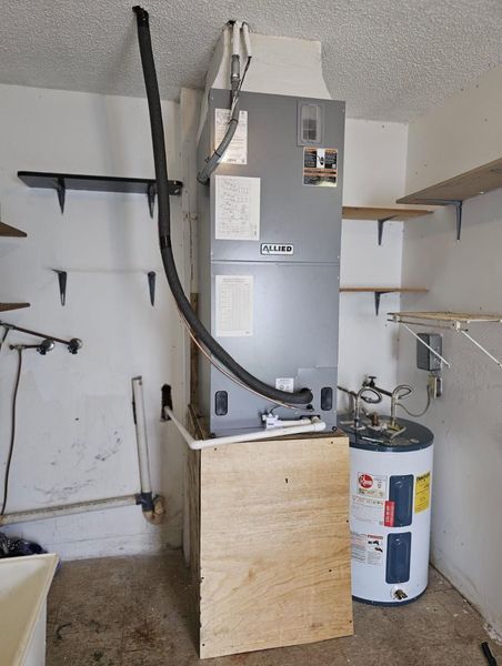 Air conditioning unit and water heater in a garage setting with wooden shelf and plywood panel.