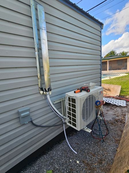 An outdoor air conditioning unit installed on a gray building. A chimney-like duct runs vertically.