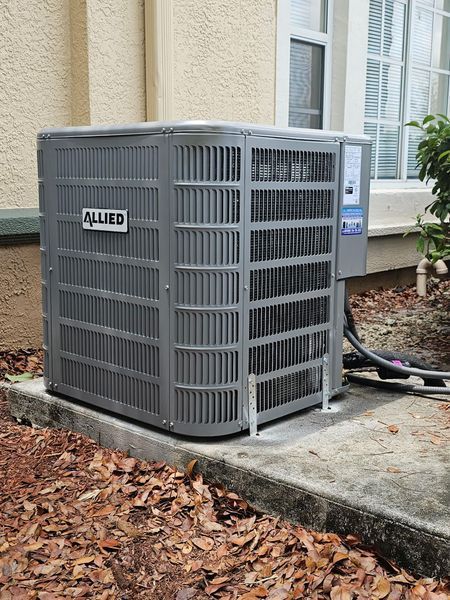 Gray Allied air conditioning unit outside a building with leaves on the ground.