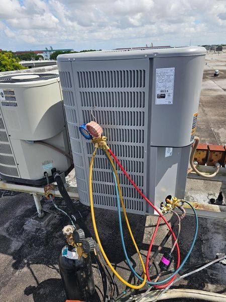 AC unit on a rooftop being serviced with gauges and hoses connected.