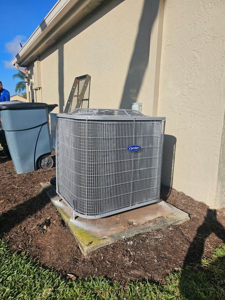 Air conditioner unit by a building, next to a trash bin and mulch.