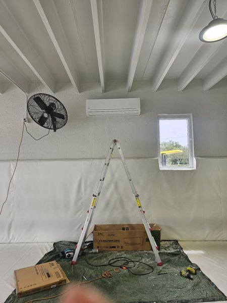 Interior with installed air conditioner and ladder under a beam ceiling, tools and boxes on the floor.