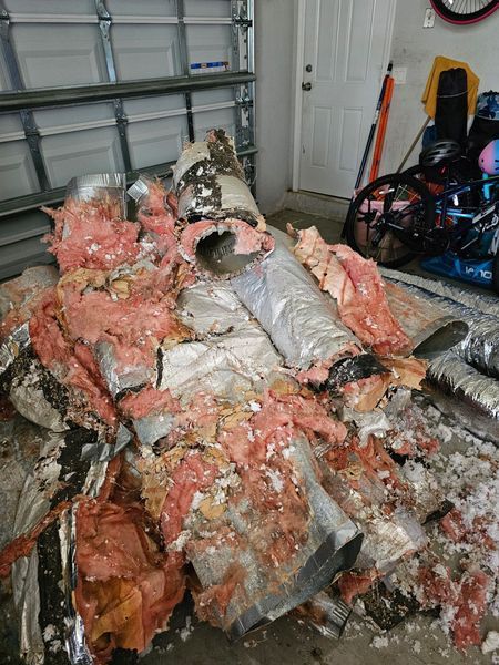 Pile of damaged HVAC ductwork in a garage, pink insulation exposed, silver tubing.