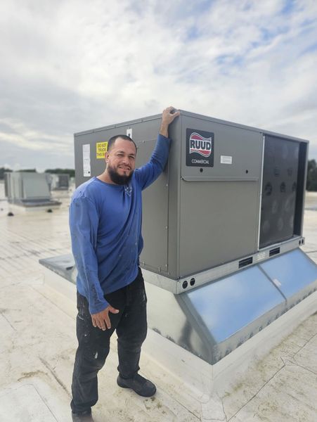 Man in blue shirt, black pants stands on a roof next to an air conditioning unit.