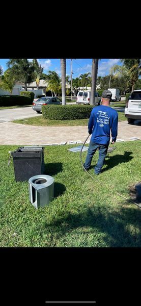 A person is spraying water on the grass with a hose. Two metal structures and a black container are in the grass.