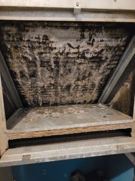 A dirty HVAC air handler interior with black and gray buildup on the fins.