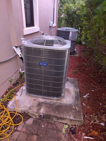 Two air conditioning units on concrete pads beside a building. Yellow cord nearby.