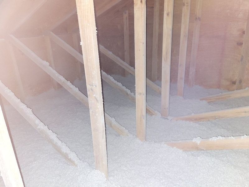 Attic interior with wooden beams and white insulation covering the floor.