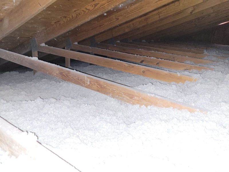 View inside an attic with wooden rafters and white insulation.