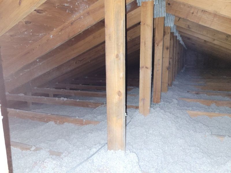 Interior view of an attic with insulation and wooden beams.