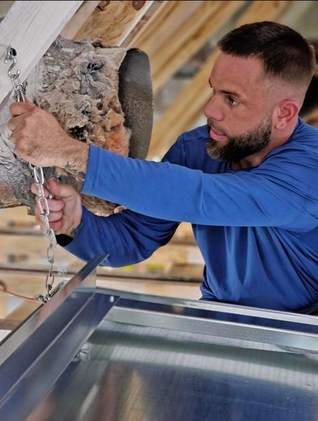 Man in blue shirt attaching a chain to a metal fixture, focused expression.