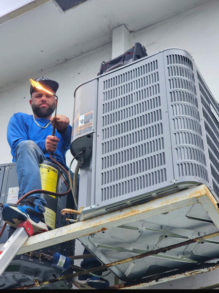 HVAC technician with torch welding on an air conditioning unit outside.