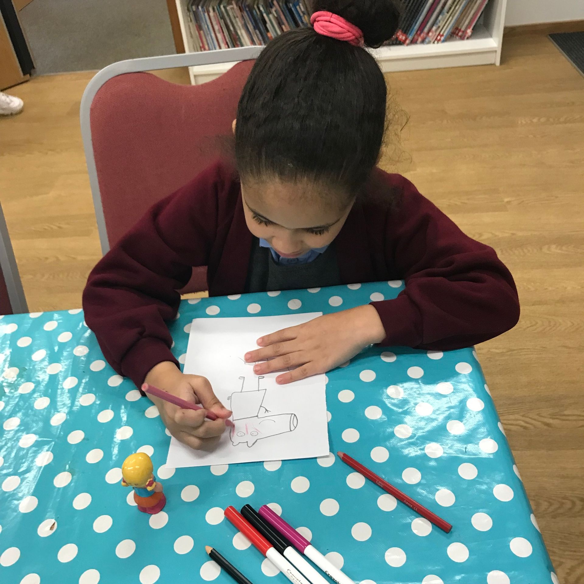 A little girl is sitting at a table drawing on a piece of paper