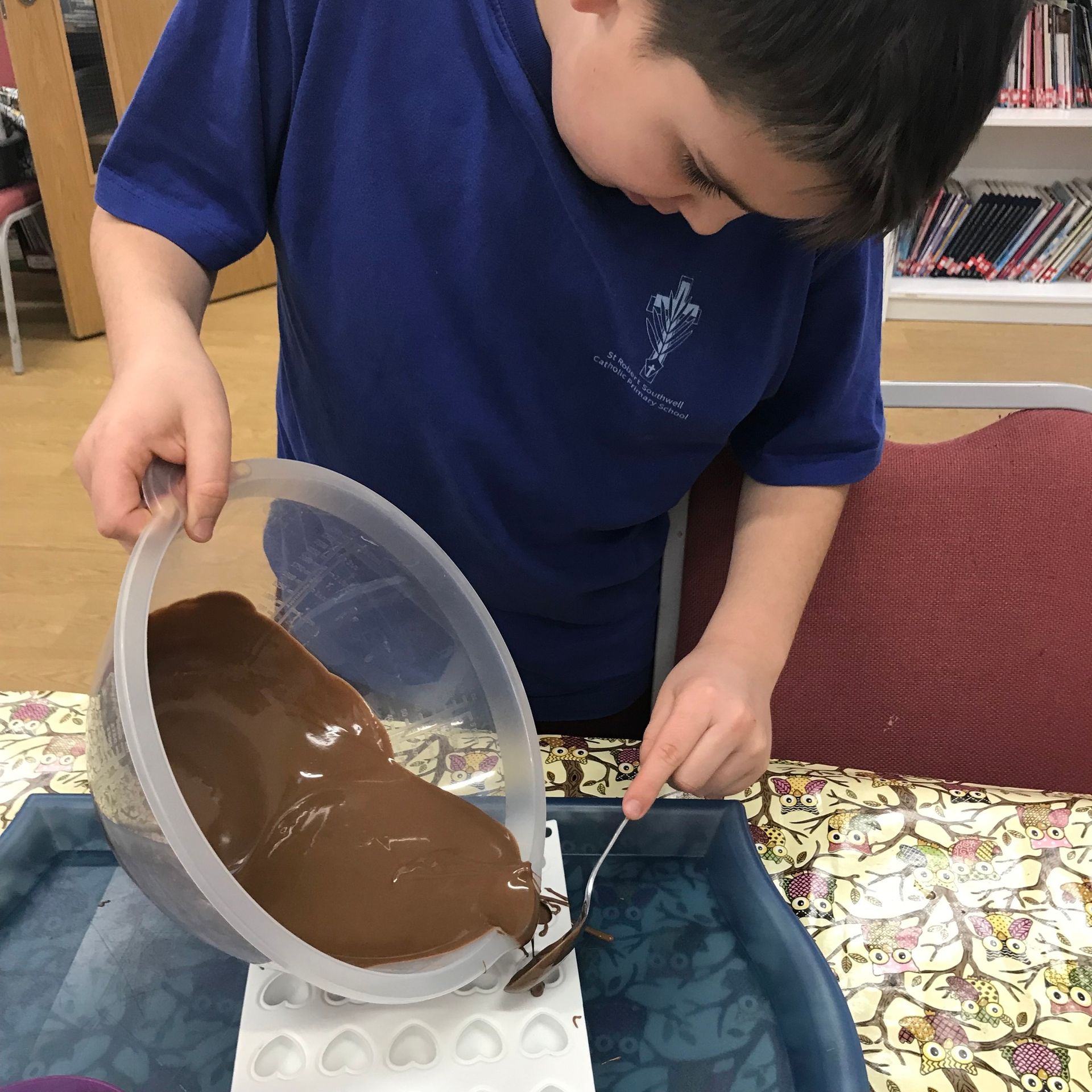 A boy in a blue shirt is pouring chocolate into a mold