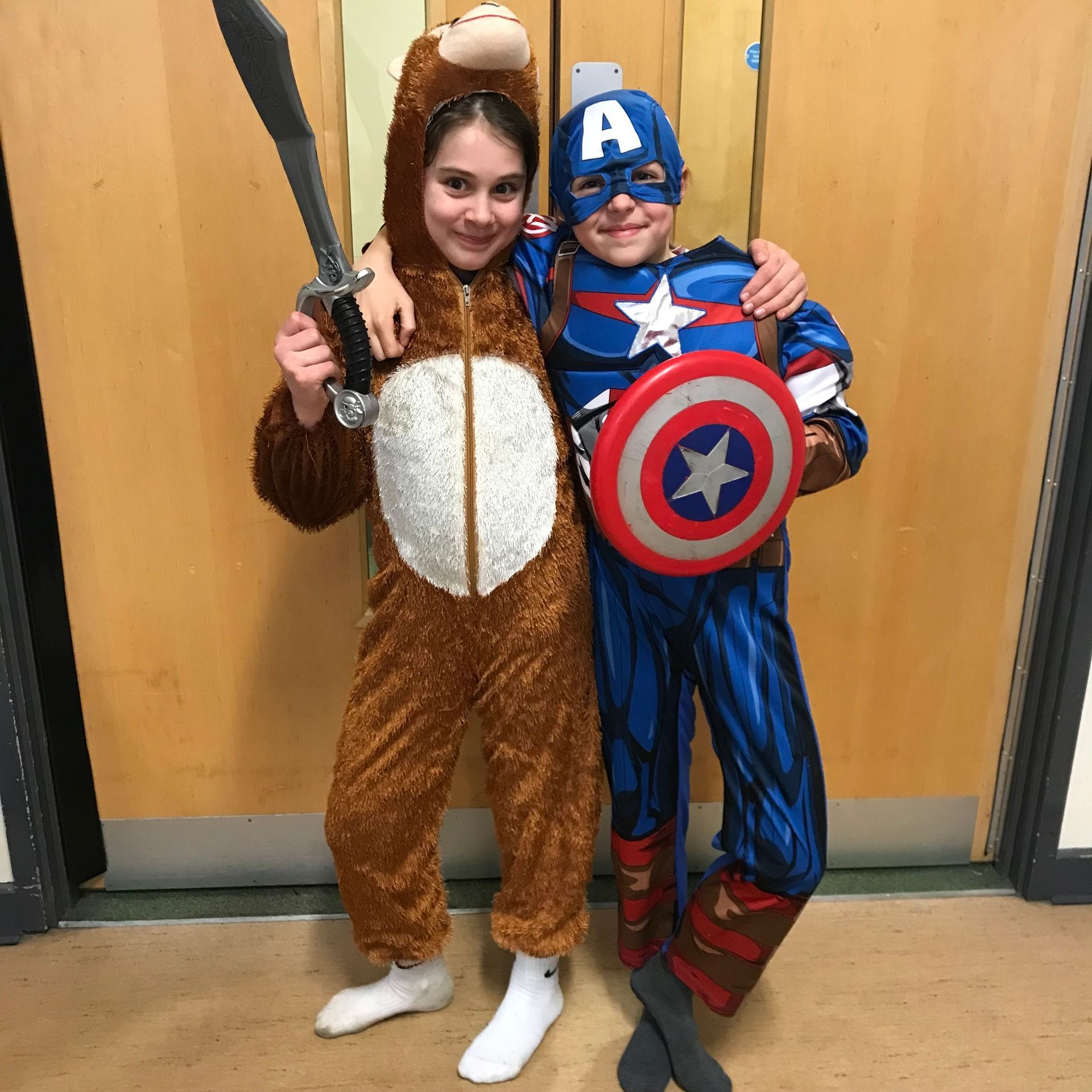 A boy in a captain america costume stands next to a girl in an animal costume