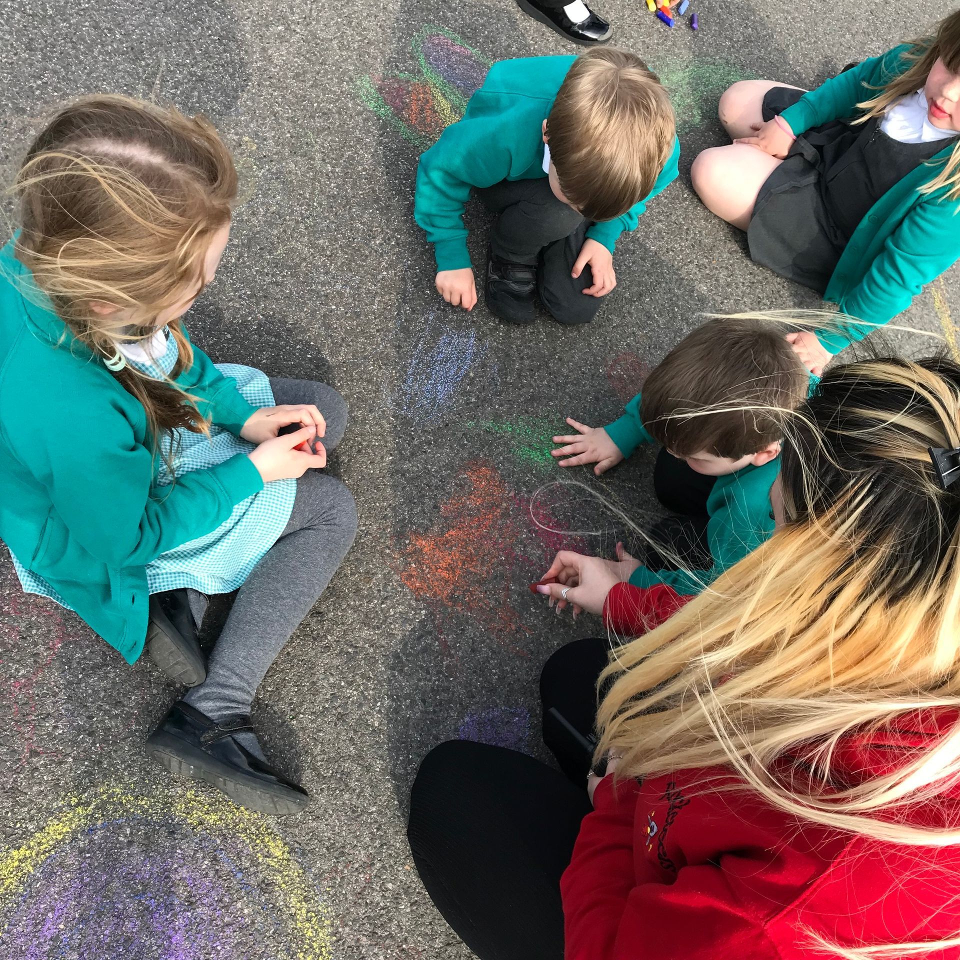 A group of children are sitting in a circle on the ground playing with chalk.
