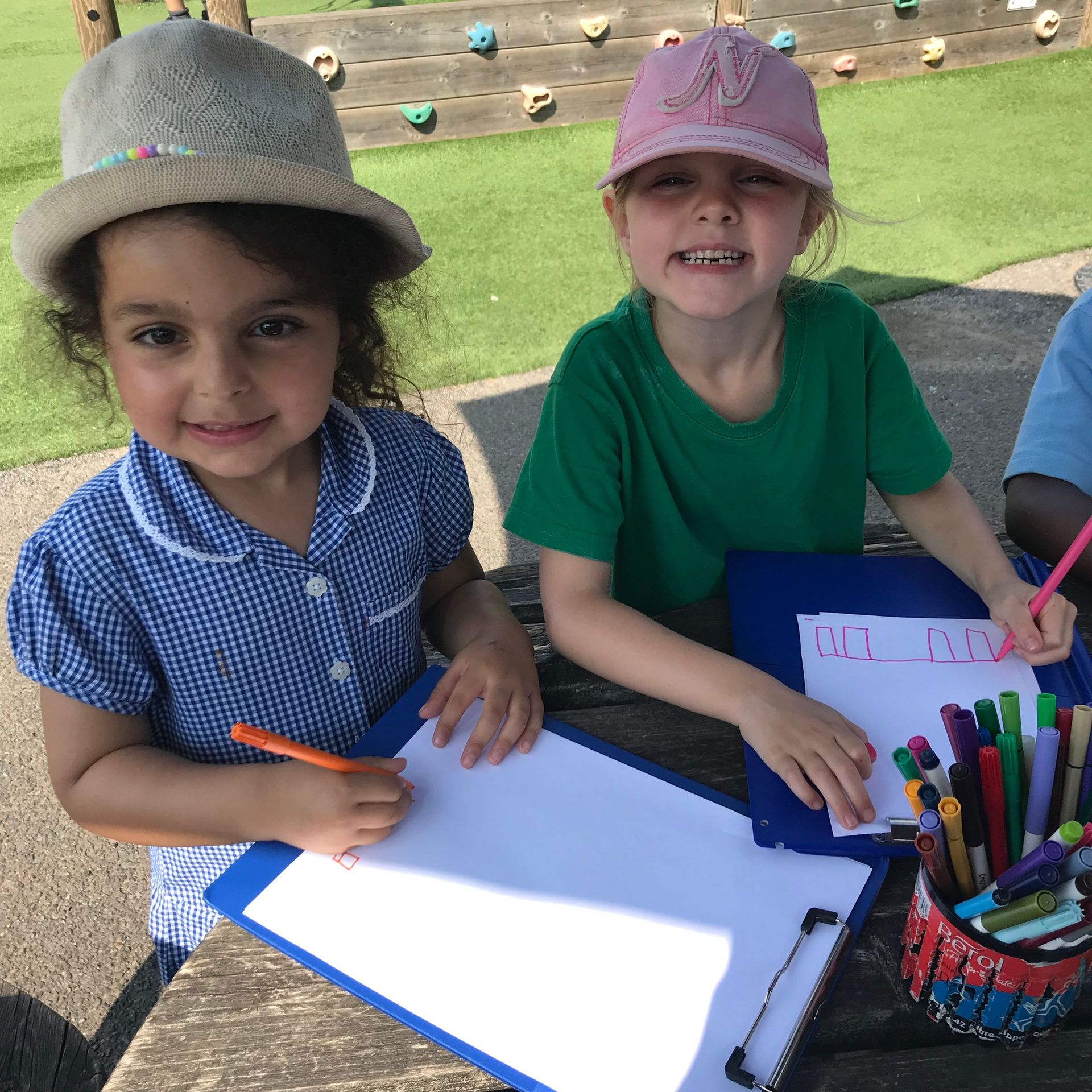Two little girls are sitting at a table with a clipboard and pencils