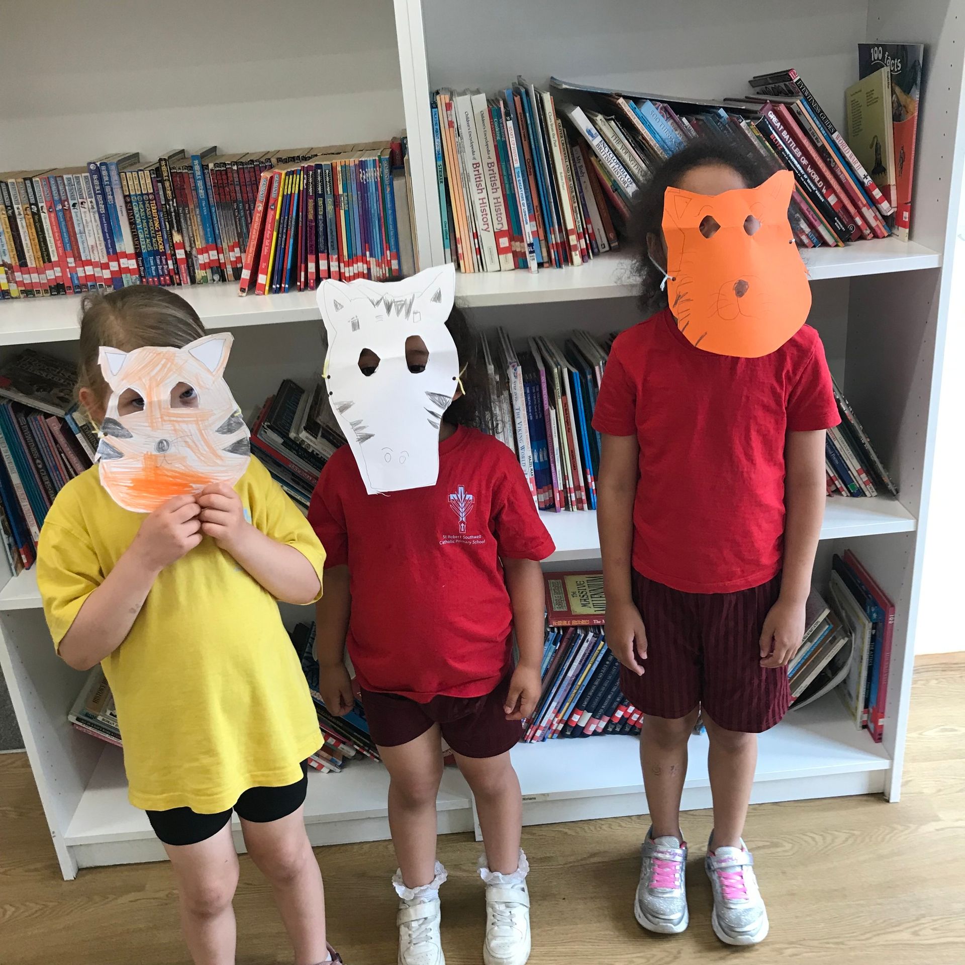 Three children wearing paper masks in front of a bookshelf