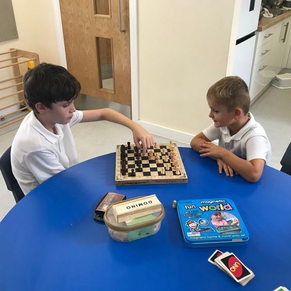 Two young boys are playing chess at a blue table
