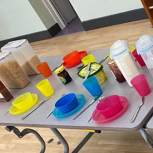 A table topped with bowls , plates , spoons , and containers of food.