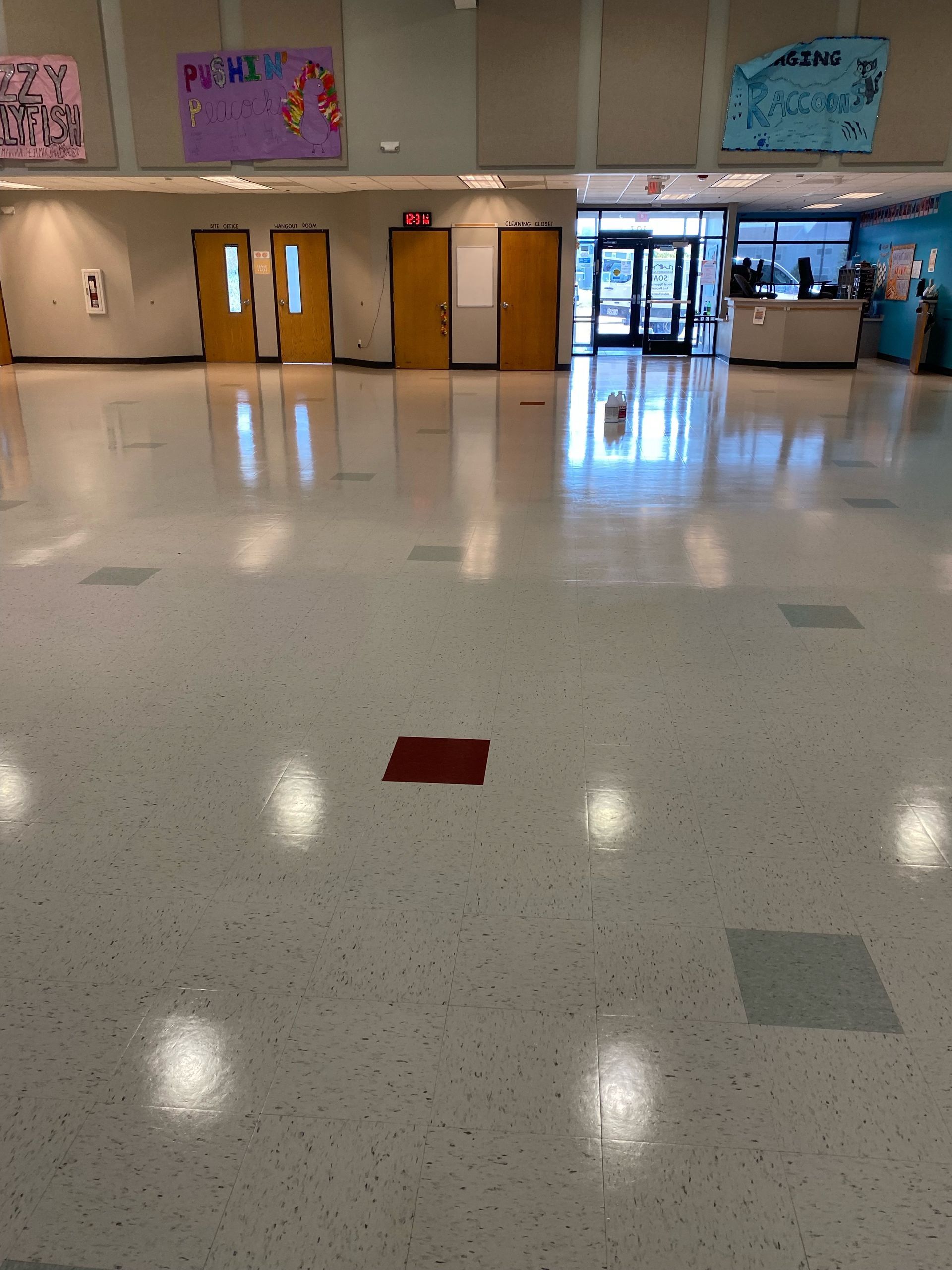 Empty school hallway with glossy tile floor, classroom doors, and a lobby area in the background