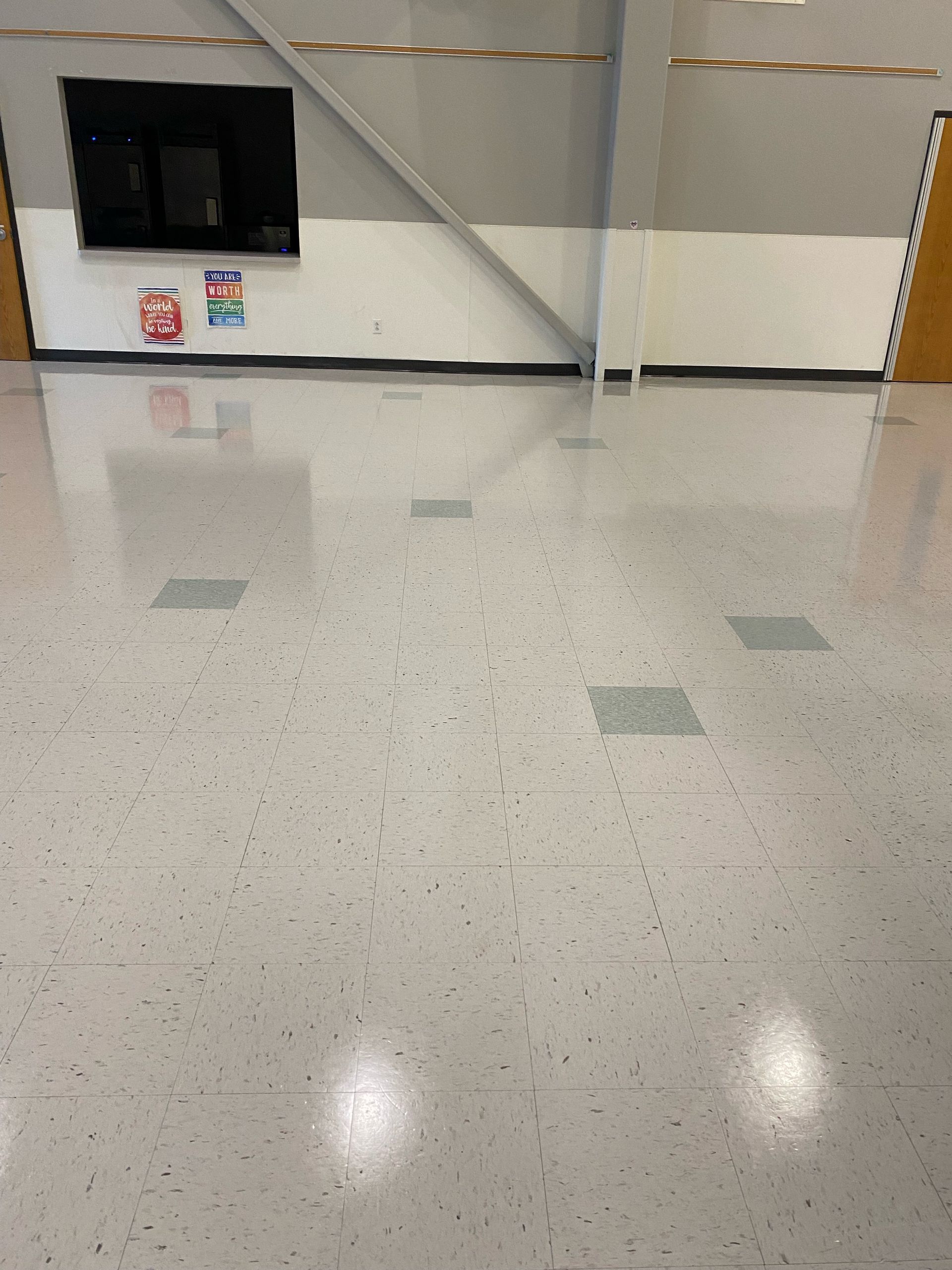 Empty airport terminal with glossy tiled floor, wall-mounted screen, and rope barriers across the back wall.