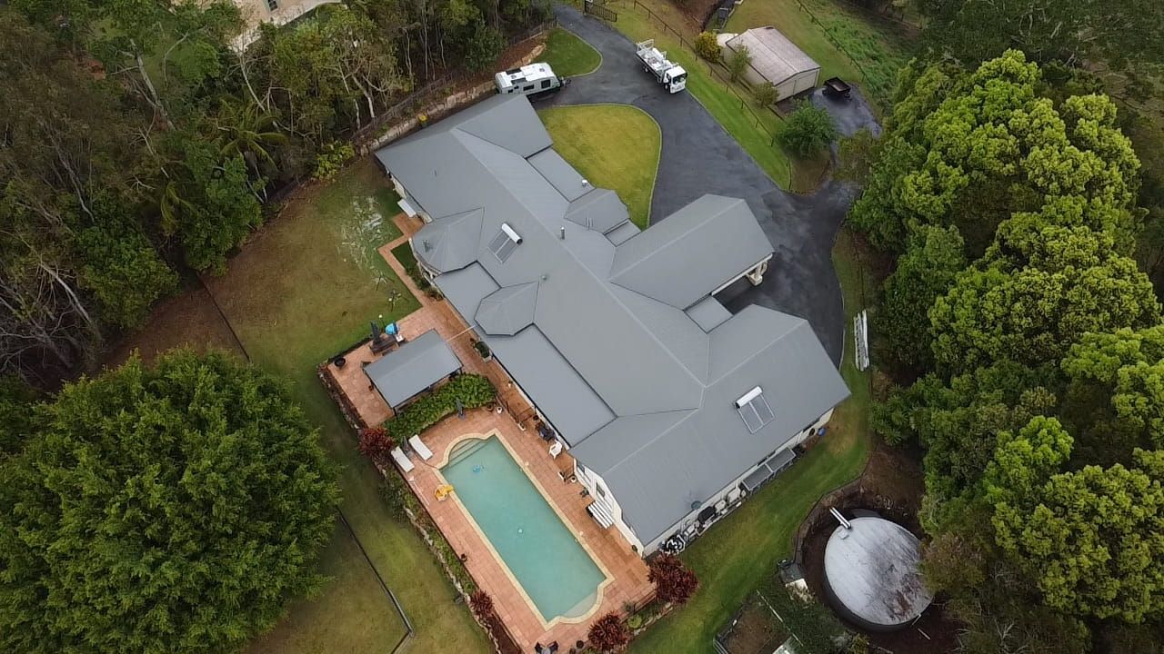 An aerial view of a house with a pool in the backyard surrounded by trees.