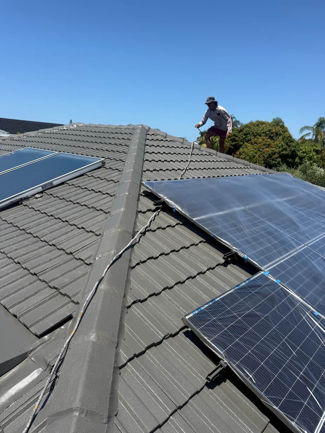 Worker installing solar panels on a gray tiled roof under a clear blue sky