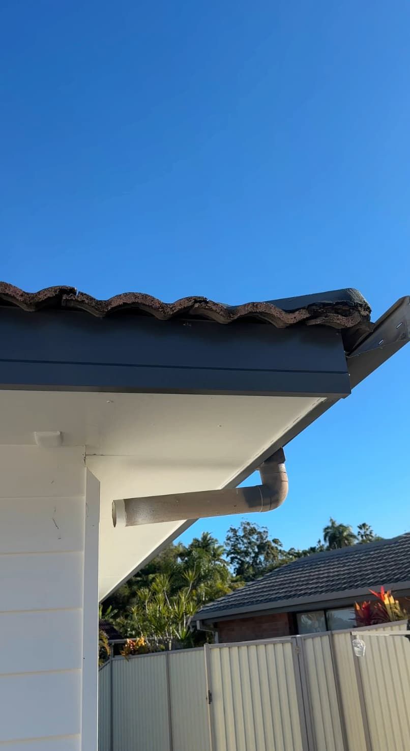 House roof eave with dark tiles against a clear blue sky, overlooking a fenced backyard