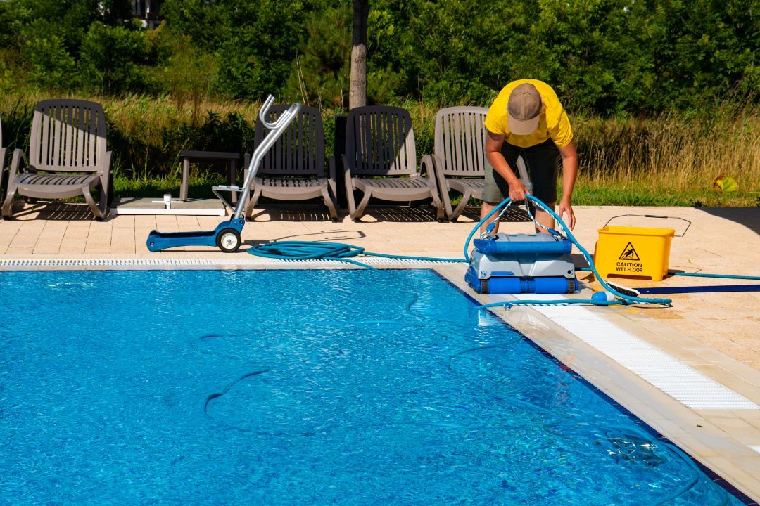 A man is cleaning a swimming pool with a vacuum cleaner.