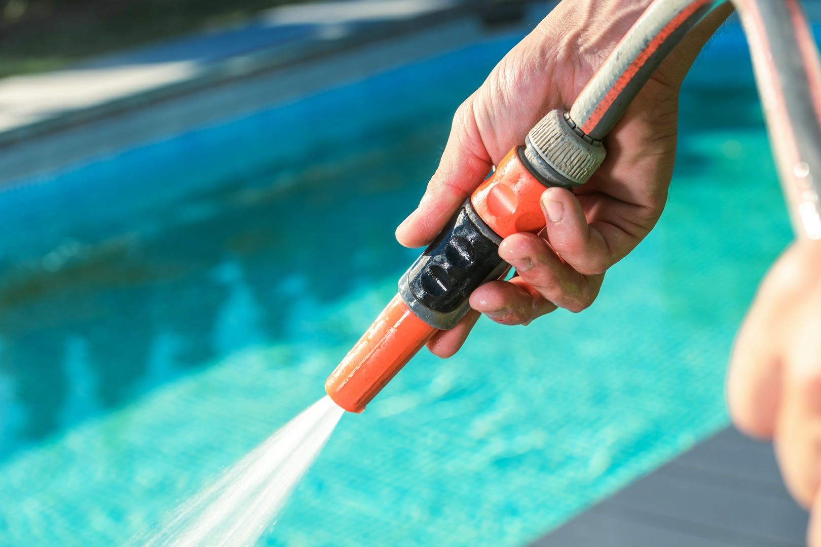 A person is spraying water from a hose into a pool.