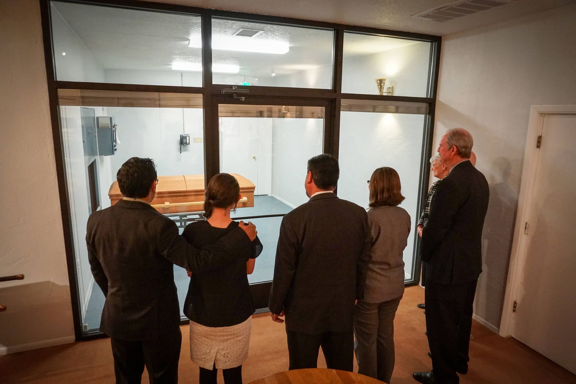 A group of people are standing in a room looking out a window at a coffin.