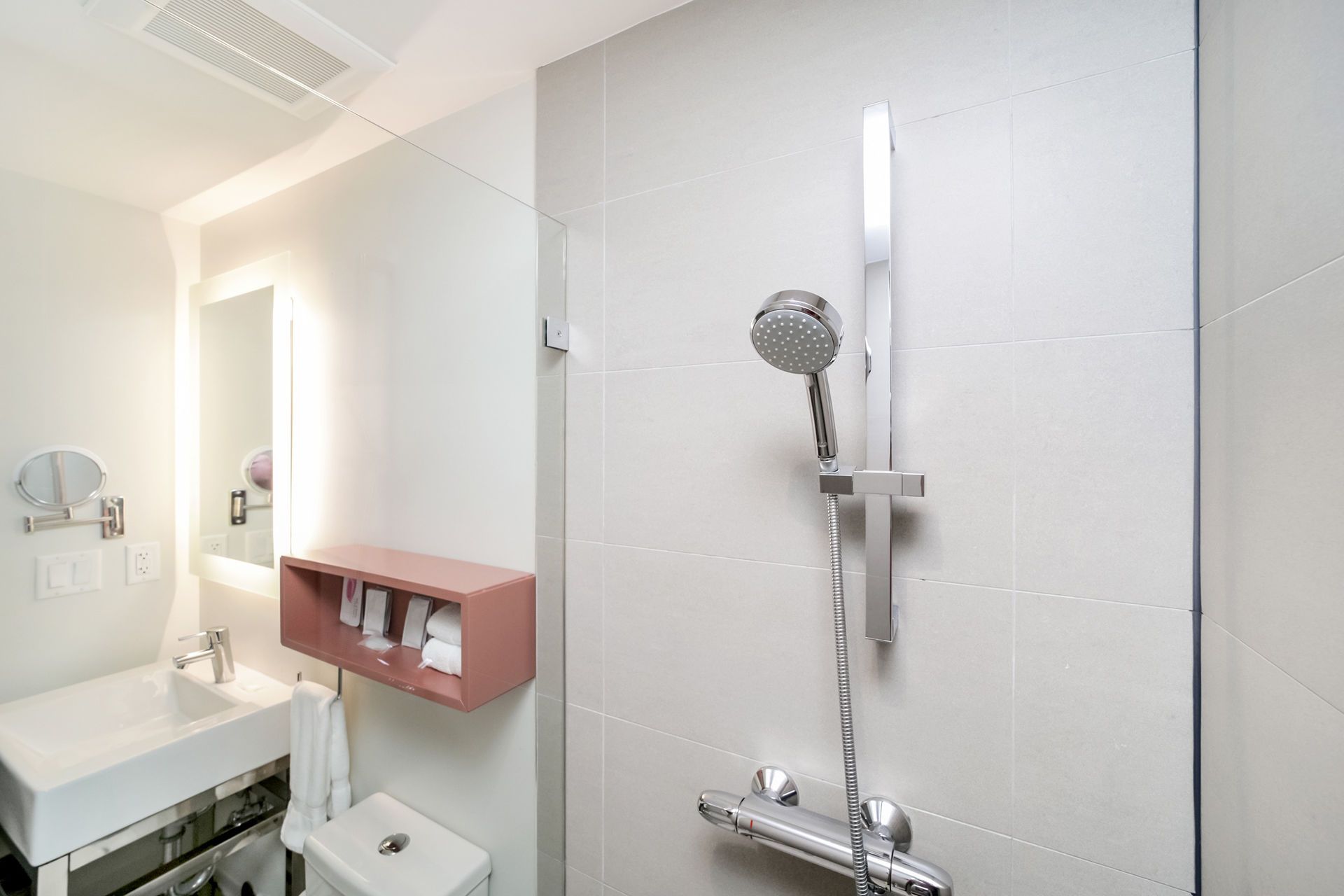 Modern bathroom with a shower, sink, mirror, and a pink shelf with toiletries.