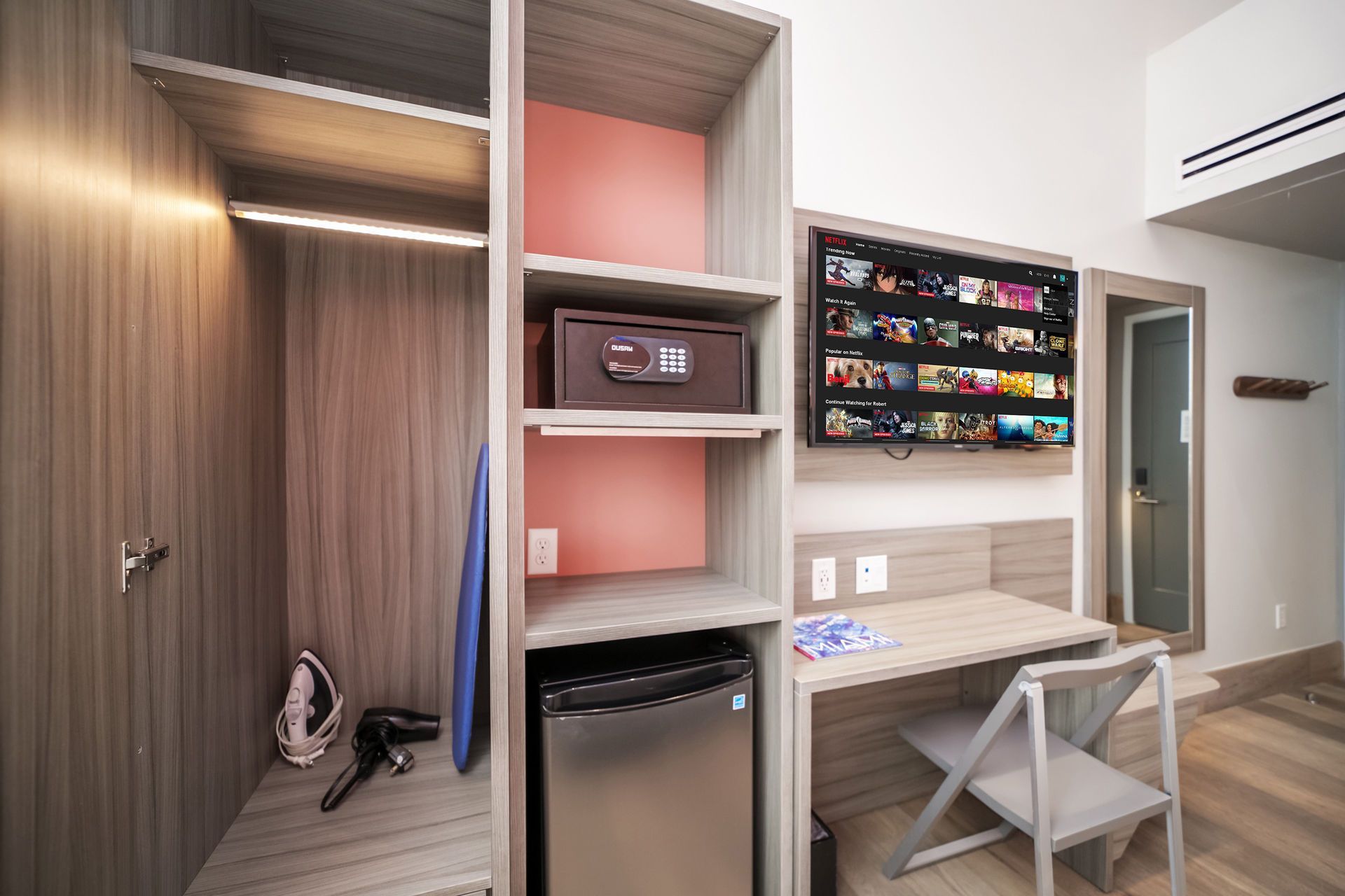 Hotel room interior with a wardrobe, TV, desk, and safe.