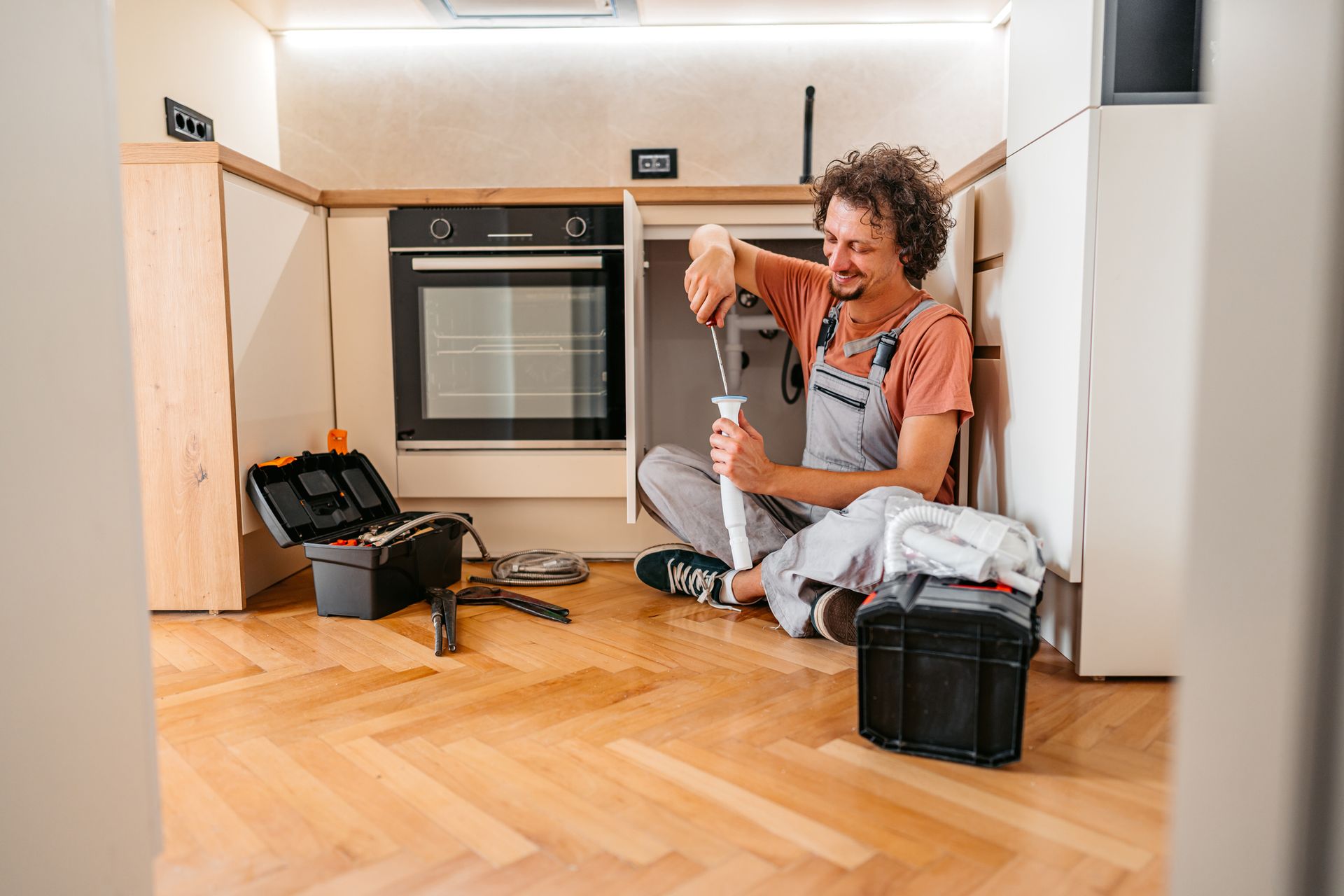 Appliance repair technician fixing kitchen oven with tools on wooden floor. Appliance repair technician fixing kitchen oven with tools on wooden floor.