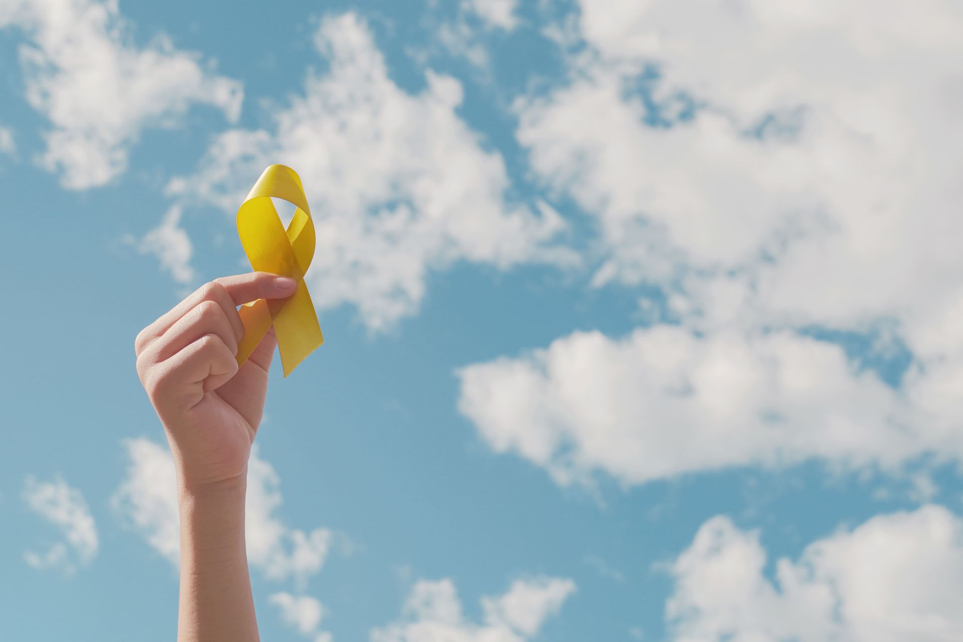 Mão segurando uma fita amarela contra um céu azul com nuvens